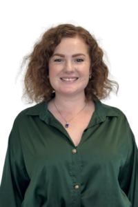 Smiling woman with curly red hair wearing a green button-down blouse, looking at the camera.